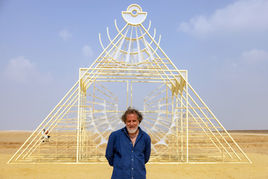Industrial photographer captures an artist before a geometric metal installation in the desert; symmetrical framing highlights industrial design.