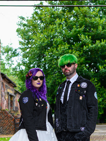 Alternative wedding couple with a punk aesthetic; bride with purple hair and groom with green hair pose in a non-traditional style.