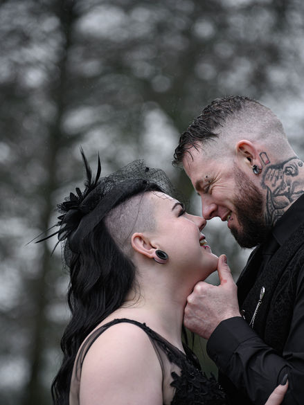 Gothic wedding couple sharing an intimate moment in the rain, with alternative fashion and tattoos adding a unique, unconventional touch.