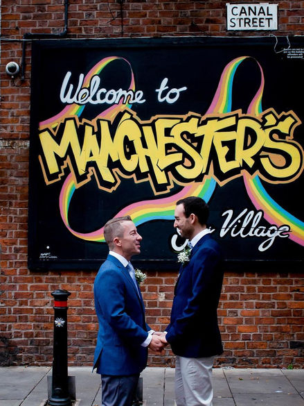 Unique wedding photography of two grooms holding hands in front of vibrant Manchester mural, celebrating love and diversity.