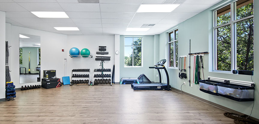 Proactive Motion Physical Therapy facility with weights, mirrors, windows, and therapy equipment including balls and bands.
