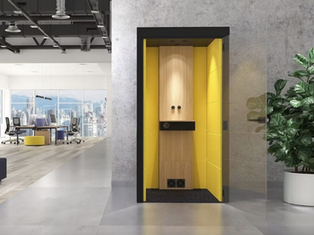 a modern office phone booth with yellow interior is being displayed in an office setting. There next to the pod.