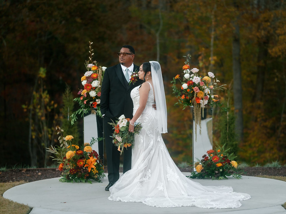 North Carolina outdoor wedding ceremony with bride and groom under floral arch featuring orange, white, and blush blooms with aisle arrangements”