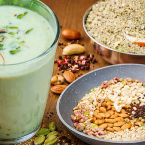 होममेड होली स्पेशल ठंडाई का गिलास, ऊपर केसर और पिस्ता गार्निश के साथ, पास में ठंडाई पाउडर और बादाम, काजू, पिस्ता, सौंफ, काली मिर्च और इलायची जैसी सामग्री