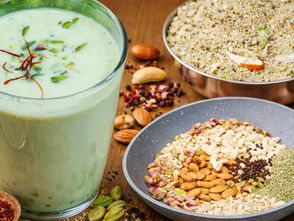 होममेड होली स्पेशल ठंडाई का गिलास, ऊपर केसर और पिस्ता गार्निश के साथ, पास में ठंडाई पाउडर और बादाम, काजू, पिस्ता, सौंफ, काली मिर्च और इलायची जैसी सामग्री