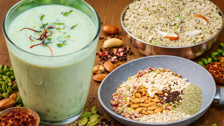 होममेड होली स्पेशल ठंडाई का गिलास, ऊपर केसर और पिस्ता गार्निश के साथ, पास में ठंडाई पाउडर और बादाम, काजू, पिस्ता, सौंफ, काली मिर्च और इलायची जैसी सामग्री