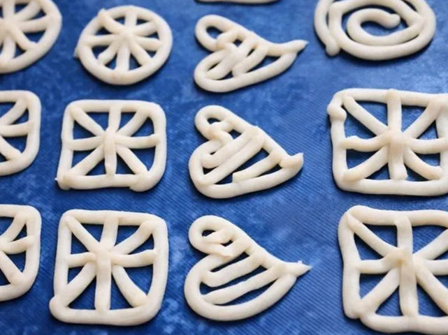 घर पर बने चावल के आटे के फ्रायम्स, जिनमें रिंग, स्क्वायर और स्पाइरल डिज़ाइन दिखाई दे रहे हैं, प्लास्टिक शीट पर सुखाए हुए