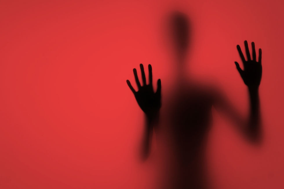 Silhouette of a person with hands pressed against a red glass surface. The blurred figure creates a mysterious, dramatic mood.