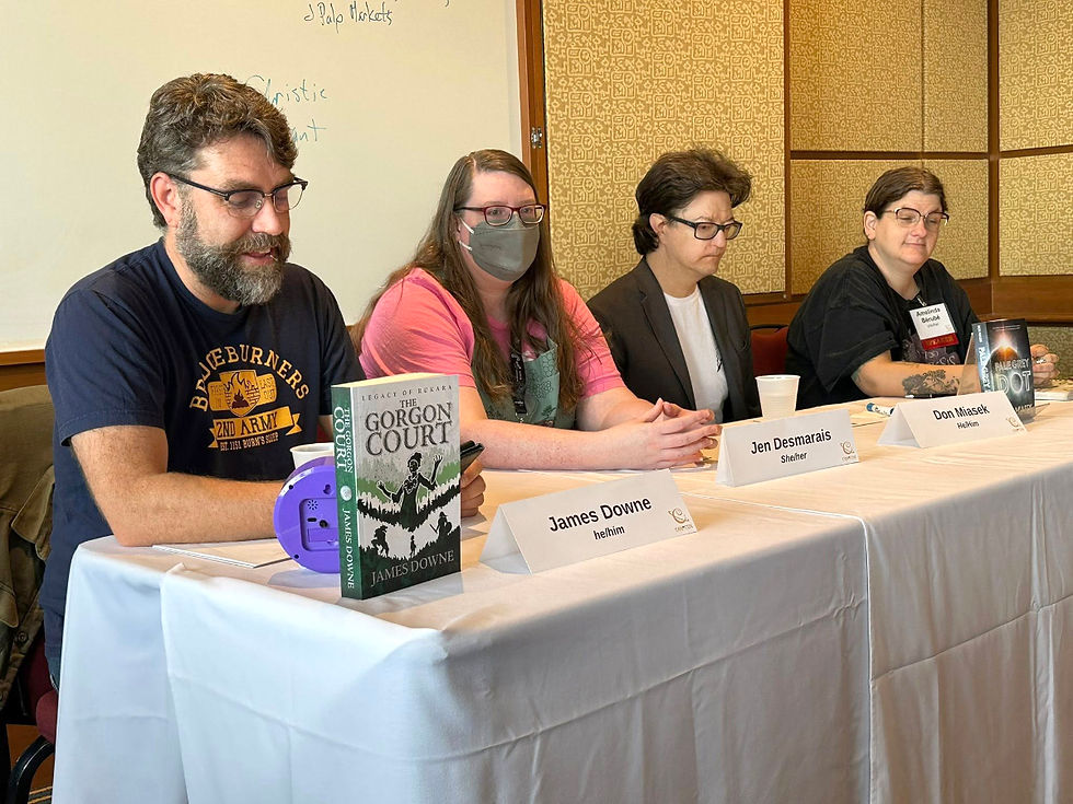 Authors at a panel discussion, seated behind a table with name cards, books displayed. Casual setting with a whiteboard in the background.