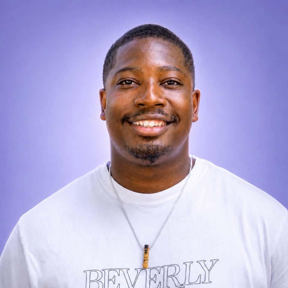 Quiy Saunders smiles in a vibrant white shirt in front of a lavendar background