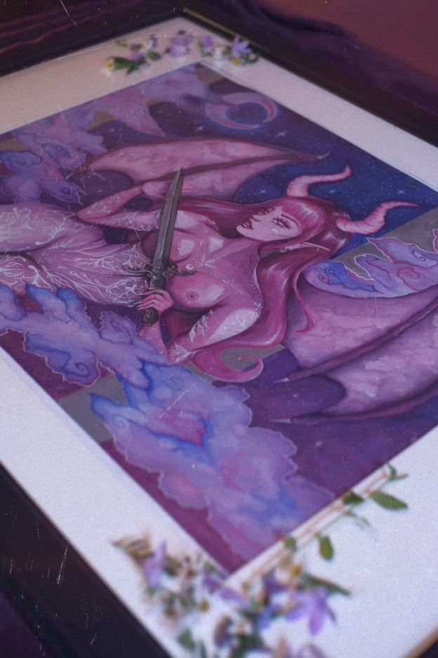 Frame canvas with flowers of a feminine winged demon woman holding a sword under a starry sky with purple clouds.
