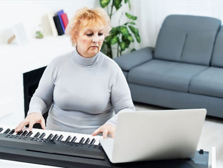 Eine Frau über 50 spielt Klavier und arbeitet gleichzeitig mit einem Laptop, auf dem eine KI-Anwendung läuft – Symbolbild für digitale Inspiration und kreative Zusammenarbeit zwischen Mensch und Technik.