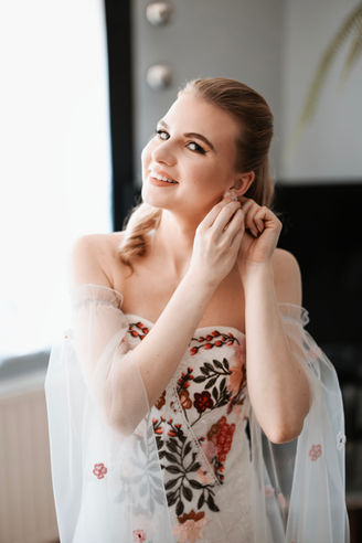 Piękna kobieta zakłada kolczyk, uśmiechając się, w jasnym, słonecznym świetle. kesjastępka-fotograf