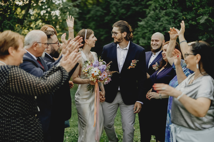 Fotograf ślubny Poznań- Uśmiechnięta para młoda idzie, ludzie klaskają, Oferta ślubna na ślubie.