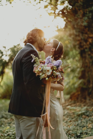 Fotograf ślubny Poznań- Uśmiechnięta para całuje się, trzymając bukiet kwiatów, Oferta ślubna w parku.