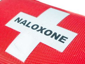 Red emergency kit pouch with a white cross and the word naloxone printed across it.