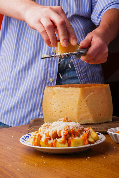 Main râpant du fromage sur un plat de pommes de terre.