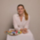 Femme blonde souriante avec une palette de peinture, face à l'appareil photo.
