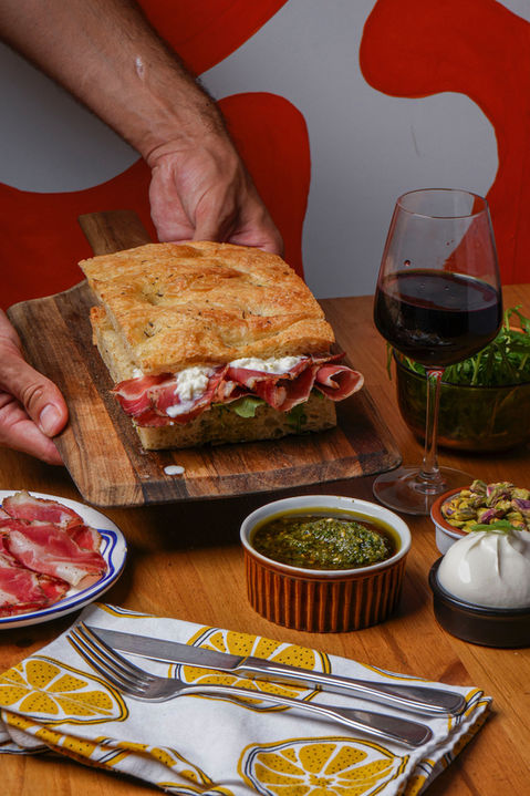 Mains présentant un sandwich focaccia, vin rouge.