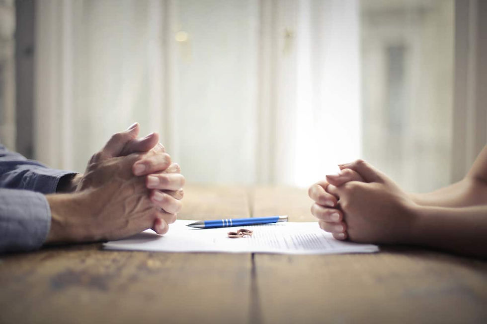 two sets of clasped hands facing each other across a table with documents between them