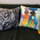 Thumbnail: "The Procession" cushion next to a colorful abstract art pillow on a dark sofa.