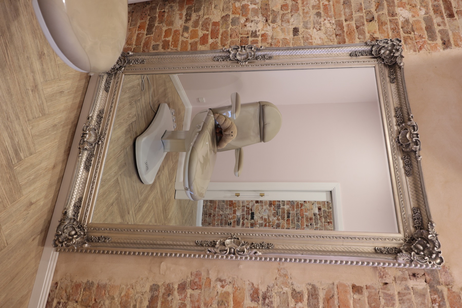 An ornate mirror framing the cream treatment chair and blush walls at By Jessi
