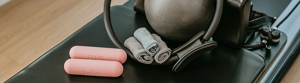 Pink Pilates toning balls, rolled gray towels, and reformer accessories arranged on a reformer bed at Living Well Pilates in Palm City, FL.
