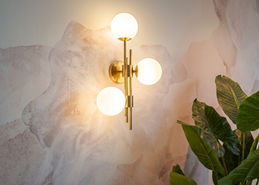 Messing design wandlamp met ronde bollen op zacht aquarelbehang in een luxe meisjeskamer.