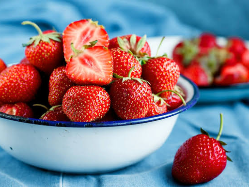 A vibrant, close-up shot of ripe red strawberries freshly harvested with green calyx leaves intact and seeds visible on the skin