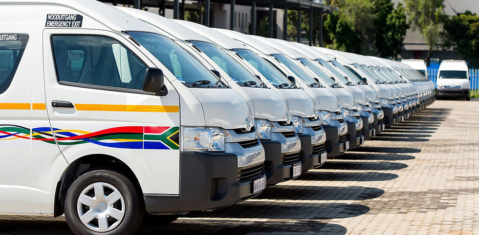 Rows of white vans lined up in a parking lot, each with colorful stripes and the South African flag on the side. Clear sky and trees in background.