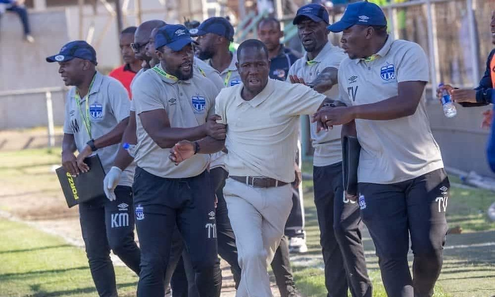 A group of men in matching sportswear escort a distressed man on a field. They hold clipboards and water bottles, appearing focused.