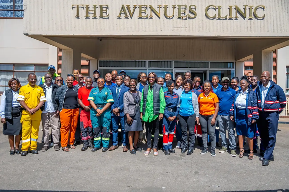 A diverse group of people in colorful uniforms stands smiling outside The Avenues Clinic. The mood is cheerful and collaborative.
