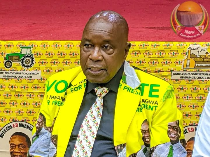 Man in yellow suit with "Vote for Mnangagwa" text, sitting against a banner featuring tractors and campaign slogans, appears serious.