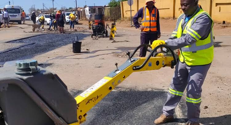Municipal workers carrying out road maintenance and pothole repairs on a highway in Zimbabwe.