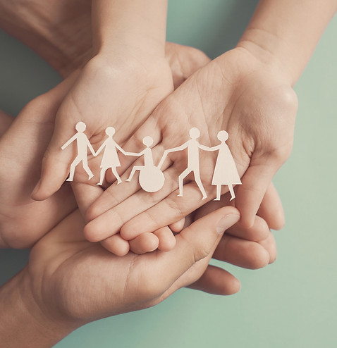 Hands holding a paper cut-out of a diverse family, including a figure in a wheelchair, symbolising support and inclusion.