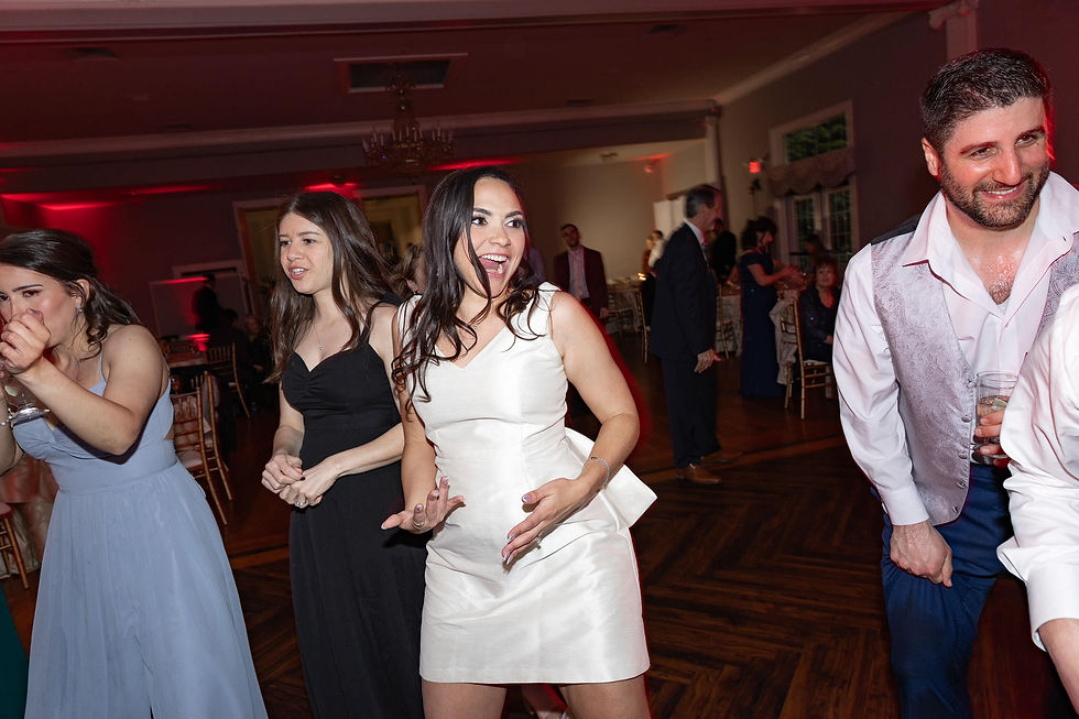 People in formal attire dance at a lively indoor event with red lighting. The mood is joyful and celebratory.