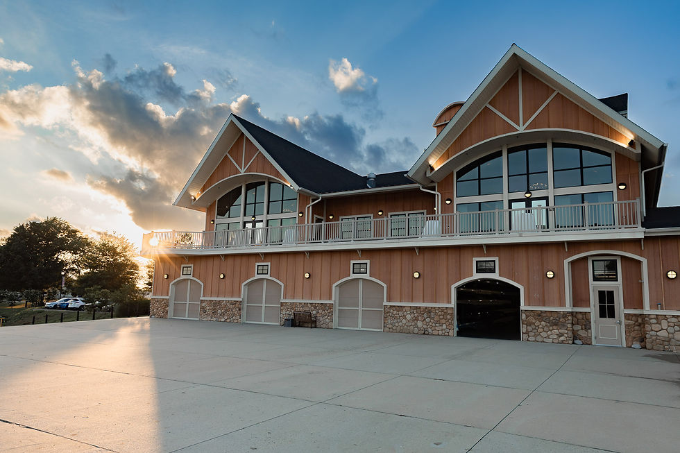 Sunset lights the Camden County Boathouse with twin gables, stone base, and a wide empty concrete courtyard under a blue cloudy sky.