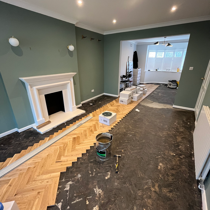 Herringbone parquet flooring being laid in freshly painted sage green living room with white fireplace by PK Decorating Wimbledon