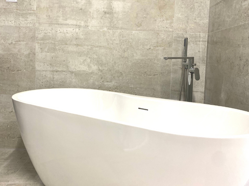 Freestanding bathtub with chrome freestanding bath tap against concrete bathroom tikes