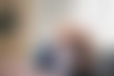 A smiling, happy senior couple sitting on a couch in their bright living room, looking at and pointing at a digital tablet together.