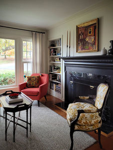 A charming cottage living room in University City, Missouri has a black fireplace, mismatched chairs, and an oil painting above the mantel.