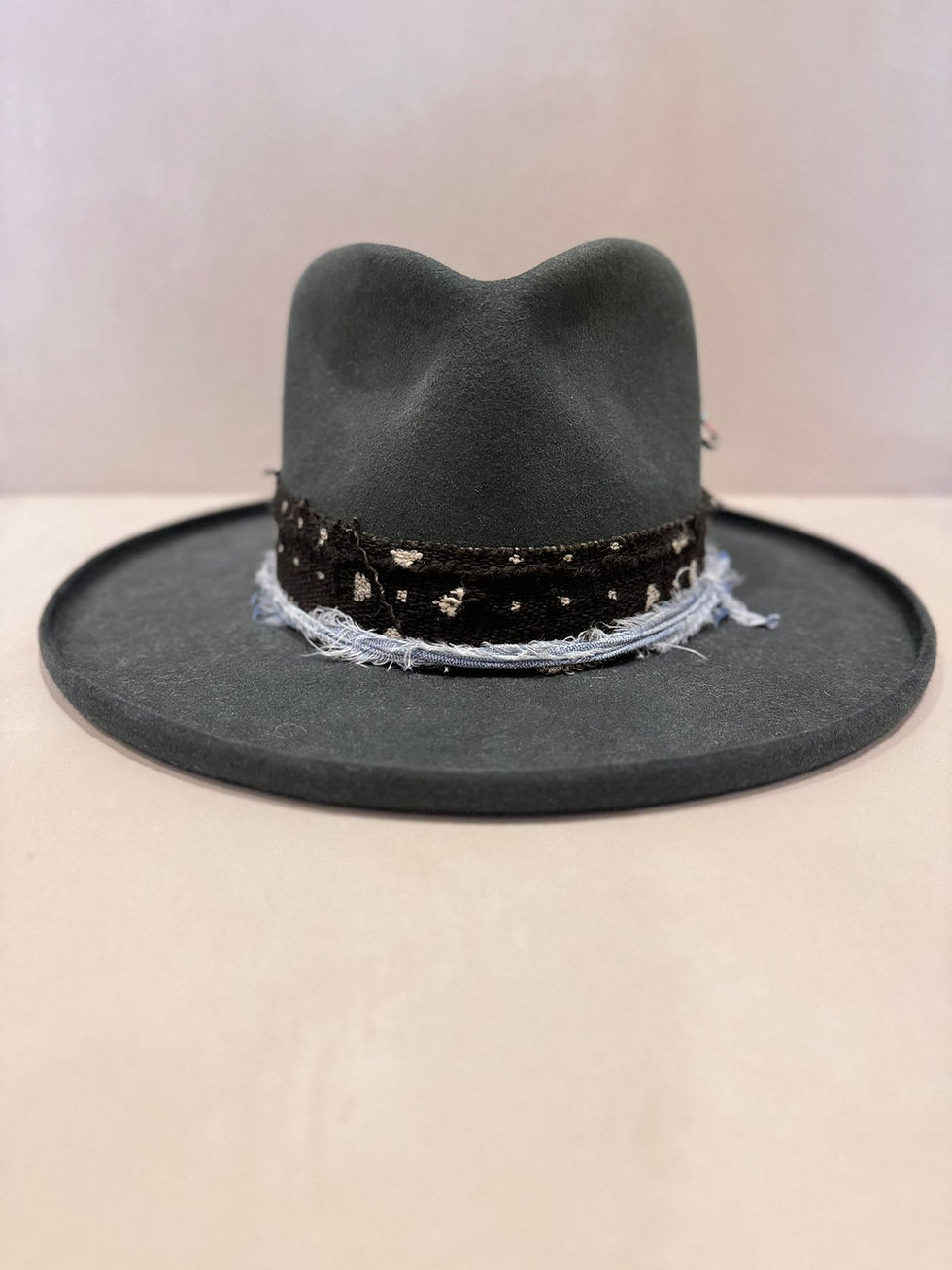 Thumbnail: A front on view of a slate grey fedora with a navy blue and light blue ribbon around the base. A kettle curl brim and signature Marcel Rodrigues safety pin embellishment