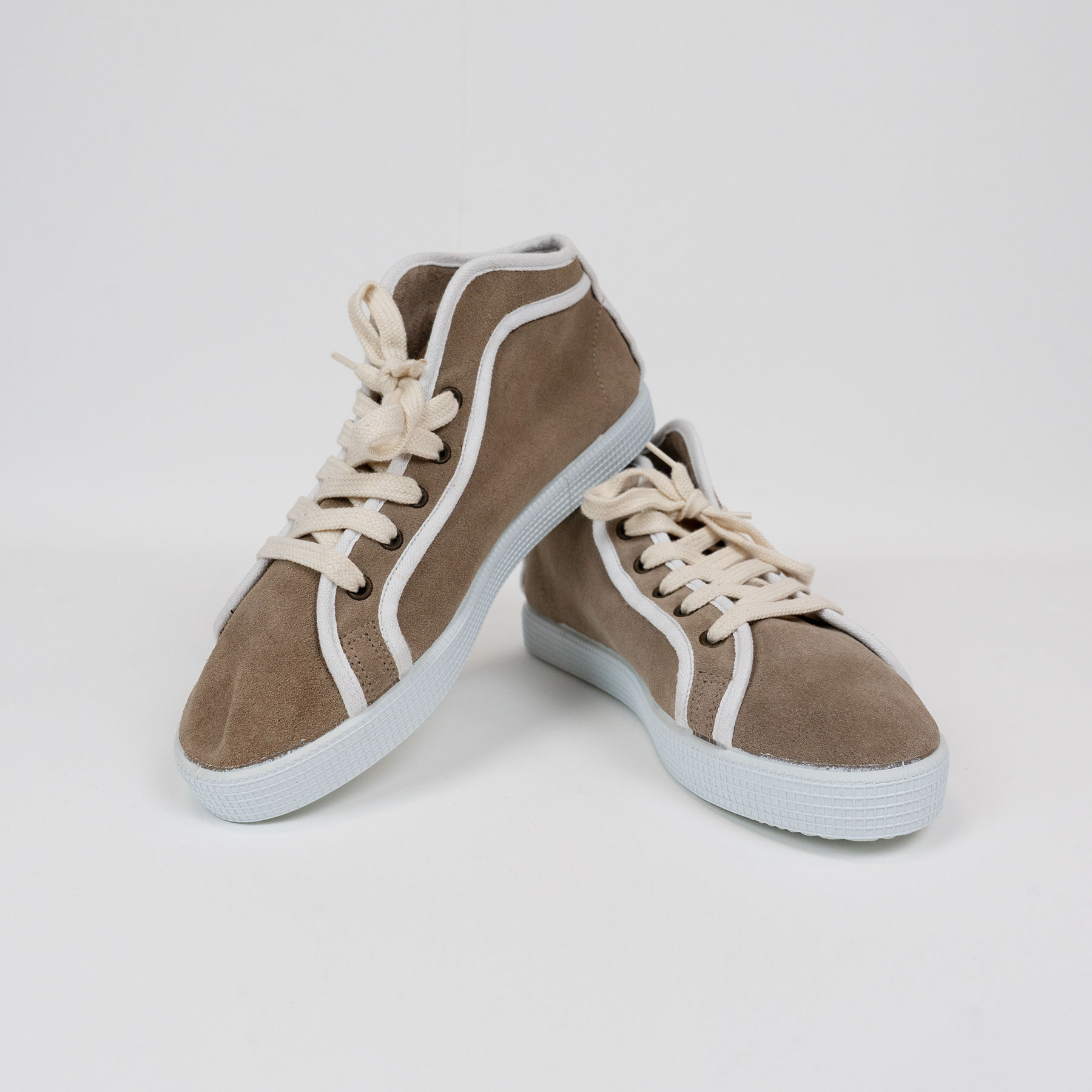 A pair of sand and white coloured high top trainers made by CaulainCourt, Paris. Here the right shoe is stacked on top of the other. 