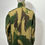 Thumbnail: The reverse view of a  mannequin wearing a British Army 1972 Denison Smock Jacket in camouflage green and brown colours. Here with the collar turned up. 