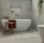 Modern bathroom design featuring a sleek white bathtub, complemented by a wooden stool adorned with green foliage and elegant glassware. The serene grey tiles and a neatly placed accent plant enhance the space's minimalist aesthetic.