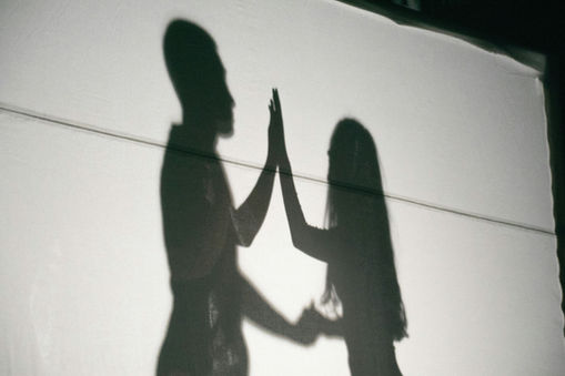 Schatten zweier Menschen, die sich gegenüberstehen und ihre Hände berühren, als Symbol für Nähe und Verbindung