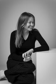 Czarno-biały portret młodej kobiety w lekkim uśmiechu, opierającej głowę na dłoni