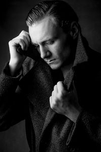 Artystyczny portret mężczyzny w czarnym płaszczu z profilu, na ciemnym tle, wykonany w studio fotograficznym w Krakowie