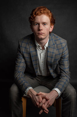 Mężczyzna siedzący frontalnie w marynarce w kratę, portret studyjny