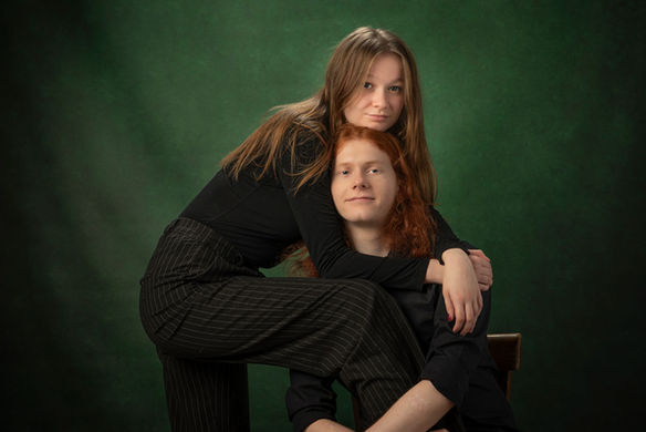 Para młodych ludzi w ciemnych ubraniach siedzi na krzesłach na tle zielonego tła studyjnego, patrząc na siebie z uśmiechem